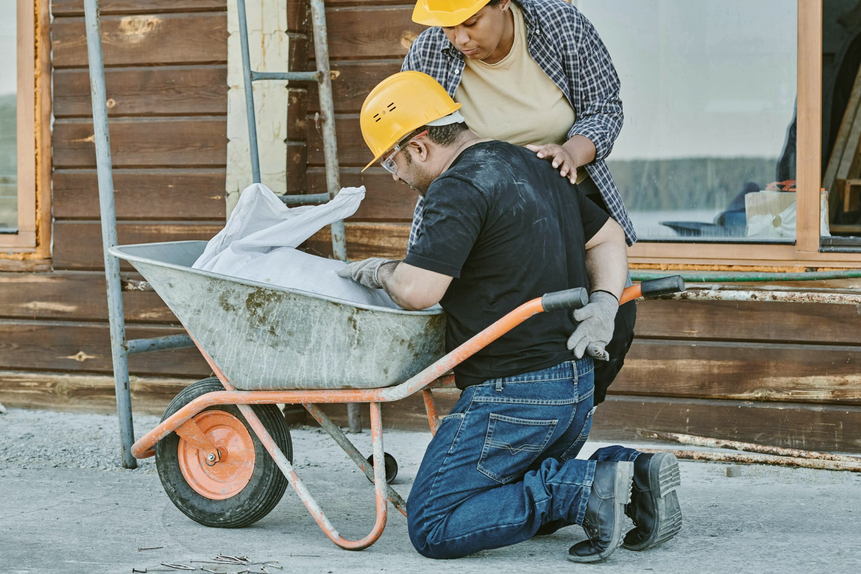 Worker kneeling by wheelbarrow outdoors.